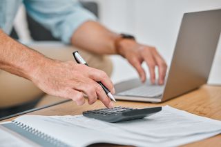 © K Davis/peopleimages.com - Adobe Stock.com Foto: Männerhände auf PC und Taschenrechner